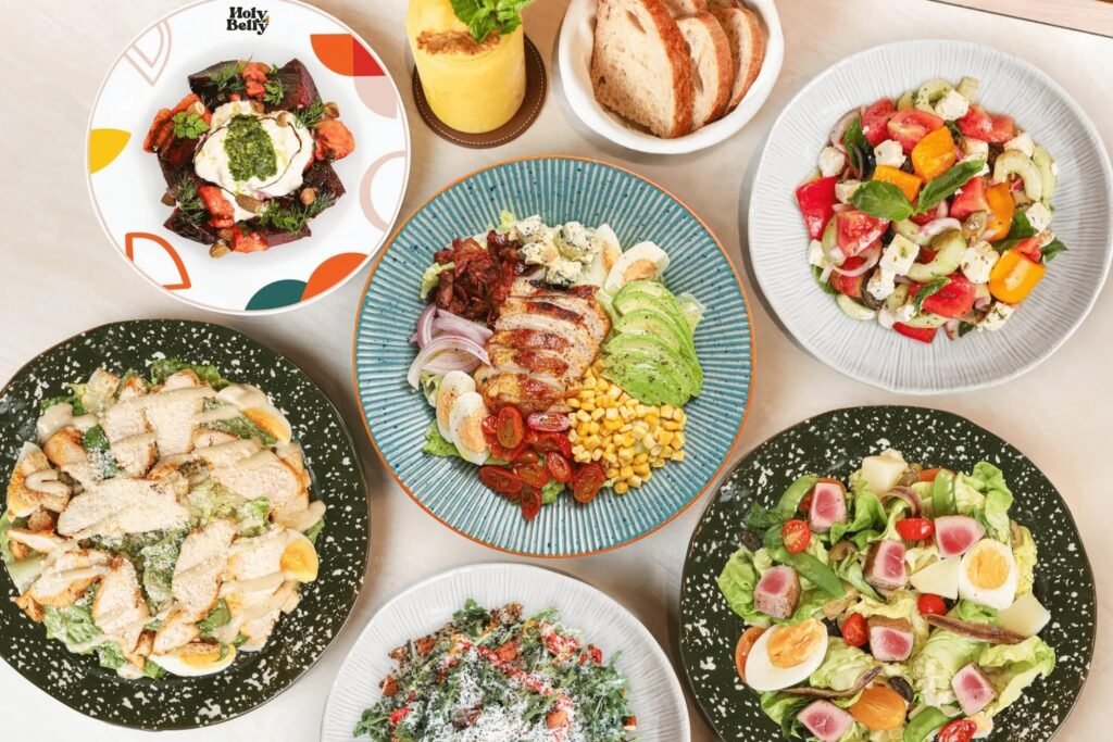 Spread of salads, grilled chicken bowl and fresh bread at Holy Belly Bangkok