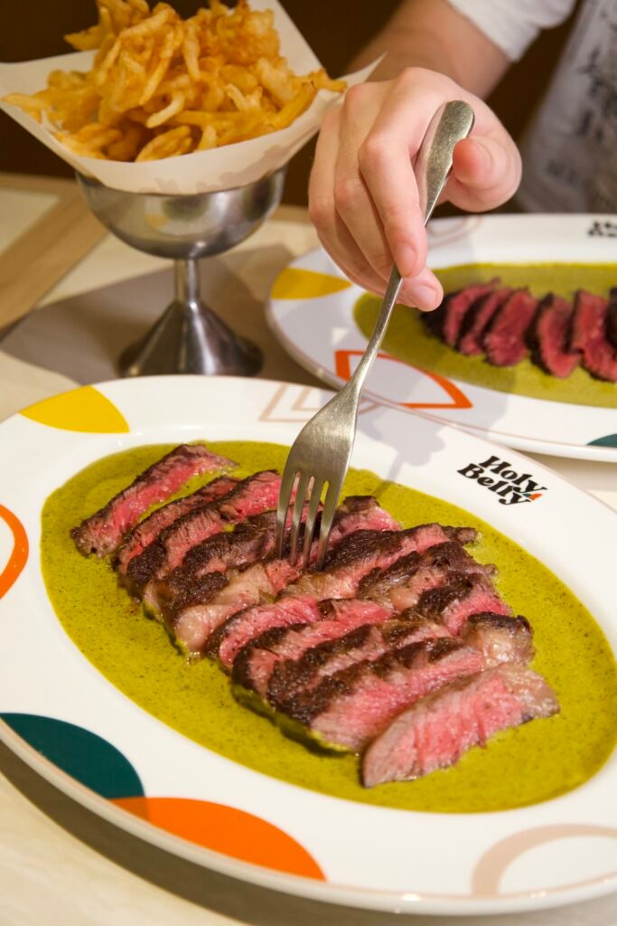 Sliced medium-rare grilled steak with green herb sauce at Holy Belly Bangkok
